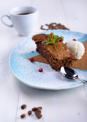Chocolate brownie with ice cream on a blue plate next to a cup of coffee. Chocolate cake with coffee