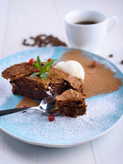 Chocolate brownie with ice cream on a blue plate next to a cup of coffee. Chocolate cake with coffee