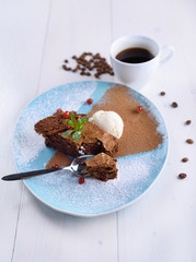 Chocolate brownie with ice cream on a blue plate next to a cup of coffee. Chocolate cake with coffee