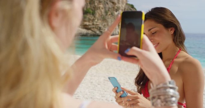 Happy teenage girl friends taking photo using mobile smart phone posing for camera being silly on tropical beach summer vacation