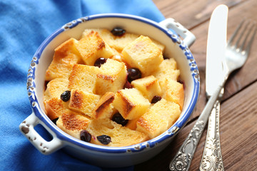Bowl with delicious bread pudding and napkin on wooden table