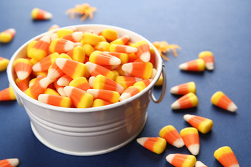 Bucket with tasty Halloween candies on color background