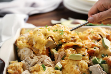 Woman taking portion of roasted chicken with cheese from casserole dish