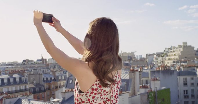 Woman taking photograph of city using smartphone from rooftop at sunset photographing Paris background view enjoying European Vacation travel adventure 