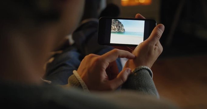 Man using smartphone browsing social media inspirational travel photos of Italy in comfort of home by warm fireplace 