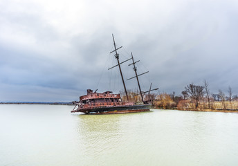 Rusty shipwreck marooned near shore on lake under a stormy blue sky