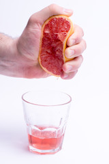 Male hand gripping grapefruit, grapefruit juice on white background