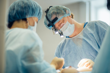 Surgeon performing cosmetic surgery on breasts in hospital operating room. Surgeon in mask wearing...