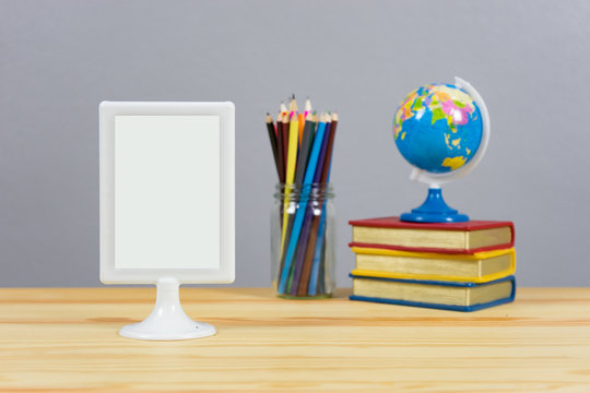 A big blank frame on the shelf leaning  and stack of book ,color pencil and globe on the school desk,knowledge background education concept,with empty space,selective focus