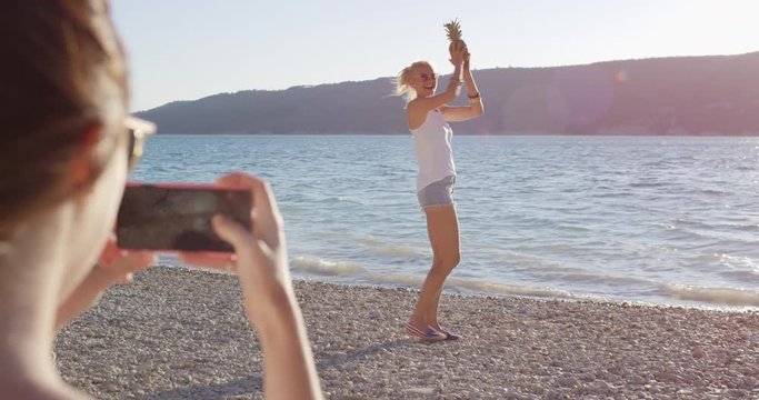 Close up attractive woman balancing pineapple on head posing for camera smiling laughing at sunset on tropical beach