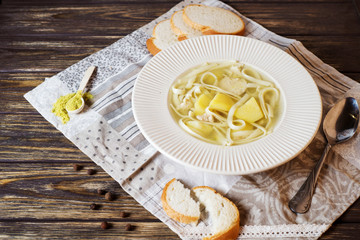 Useful, hearty and healthy lunch, chicken soup with homemade noodles, potatoes, spices and white fresh bread on a wooden background 