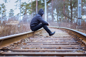 A lonely man sits on the railway, despair, autumn