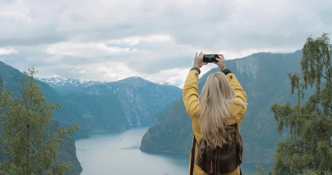 Woman taking photograph fjords with smartphone photographing scenic landscape from high up nature background view enjoying Norway vacation travel adventure
