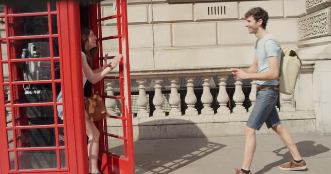 Tourist couple taking photograph of each other red london phone booth while sightseeing making funny faces enjoying European summer holiday travel vacation adventure