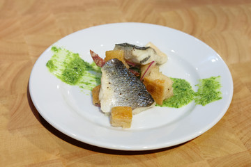 Tasty fish with crackers and green sauce on plate on wooden background. Selective focus photo.