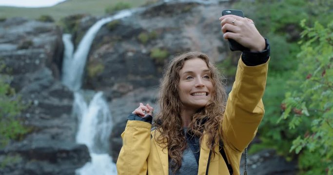 Woman hiker taking selfie photo of waterfall with smartphone Girl photographing scenic landscape nature background view enjoying vacation travel adventure