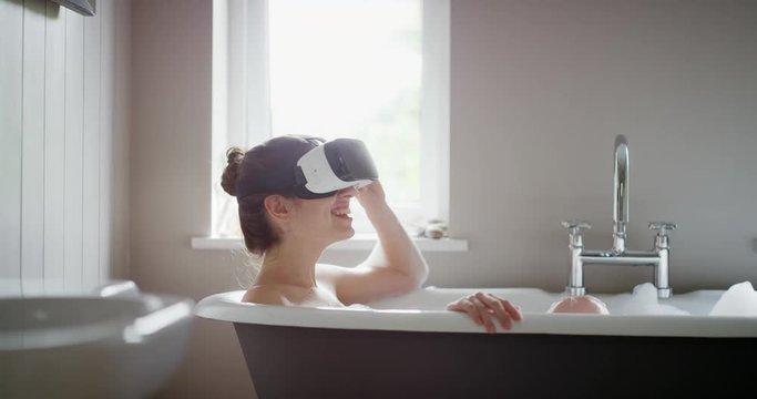 Young woman wearing virtual reality headset relaxing in bubble bath bathtub watching 360 video immersive concept mindfulness lifestyle
