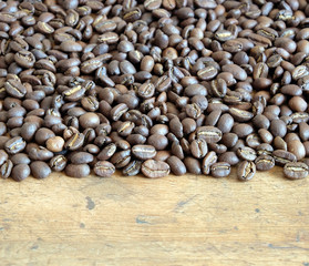 Lot of scattered roasted coffee beans on an old wooden table front view