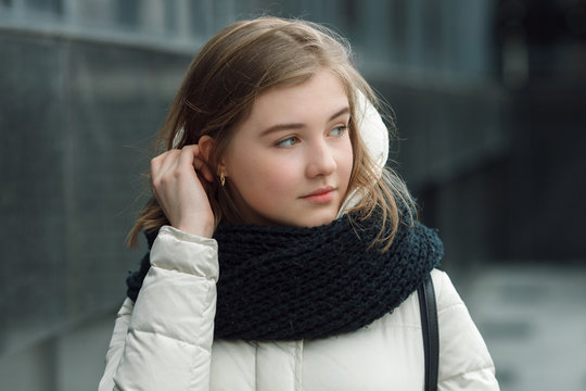 City portrait of young beautiful blonde stylish girl posing in spring fall outdoors in white coat black knitted scarf. Vintage filter film saturated colors. Emotion demonstration concept.