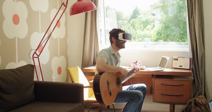 Young Man wearing virtual reality headset learning to play guitar instrument at home watching 360 video imagination concept in retro styled modern apartment