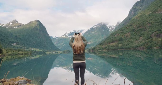 Woman taking photograph of perfect lake reflection smartphone photographing scenic landscape nature background view enjoying vacation travel adventure Norway
