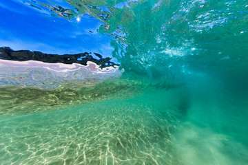 An underwater shot of a wave breaking in pristine, clear turquoise water over a sand bottom at a beautiful beach in Australia.