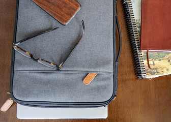 grey laptop case sits on brown table next to old book and notepad and journal ready for digital...