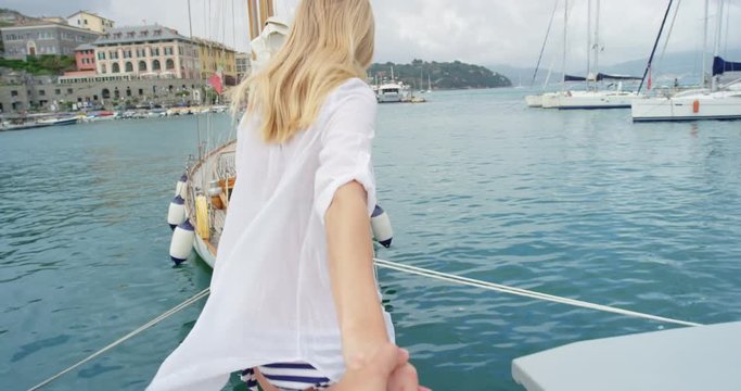 Beautiful couple holding hands woman leading boyfriend onto luxury wooden yacht sailboat POV travel concept