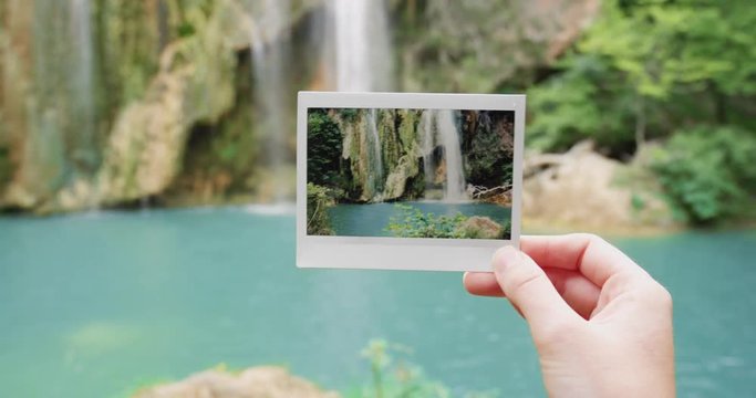 Hand holding instant photo in front of waterfall