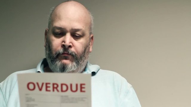 Depressed man looking at overdue bill, then looks at screen