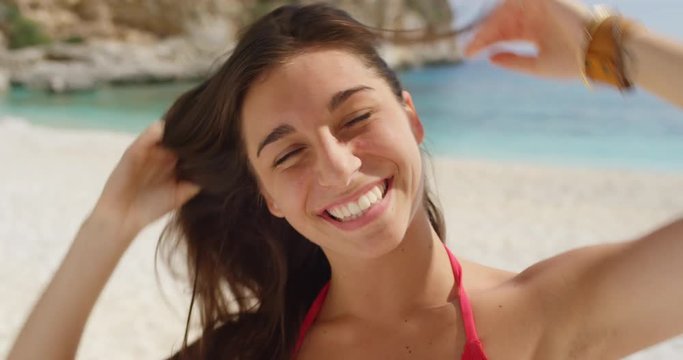 Close up portrait of beautiful young woman smiling laughing tying up hair on tropical beach slow motion