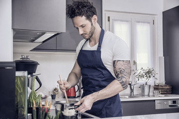 Handsome muscular man in kitchen at home, cooking at the stove