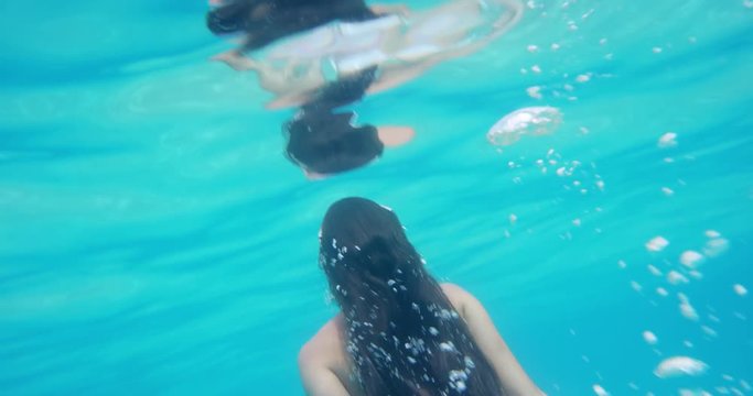 Woman swimming underwater in slow motion wearing white bikini diving down in clear blue tropical water