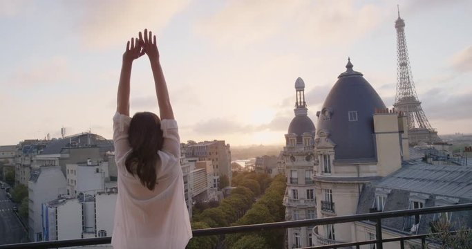 Young tourist woman stretching in morning on hotel balcony with view of Eiffel Tower Paris arms raised enjoying european travel adventure celebrating beautiful city sightseeing exploration