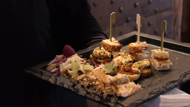 Close up of appetizer snack black tray being held by a woman in dark clothes in a restaurant, blurred background