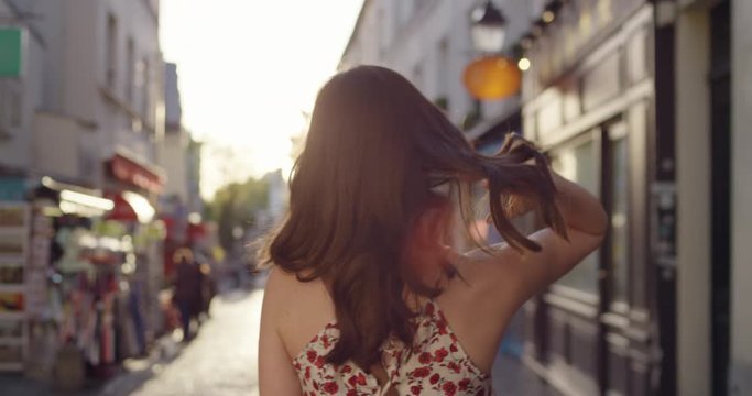 Rear view woman walking through European street at sunset wearing pretty floral summer dress sunshine lens flare confident girl exploring local Paris enjoying holiday travel vacation adventure