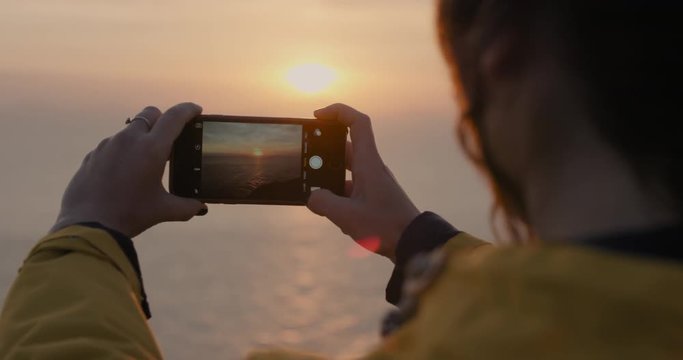Close up Woman taking photo of sunset with smartphone Girl photographing sunrise picture of ocean view with soft light lens flare landscape nature background enjoying vacation travel adventure 