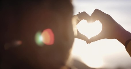 Beautiful Woman making heart shape with hands at sunset Girl holding up love symbol gesture with orange sun flare 