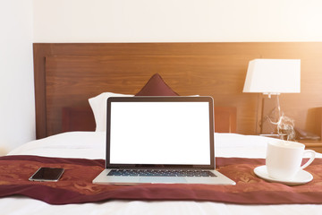 Front view of laptop computer with blank screen on bed with smartphone and coffee at morning.