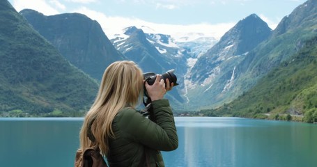 Professional photographer Woman taking photograph of valley with DSLR wearing backpack photographing scenic landscape nature background view enjoying vacation travel adventure Norway