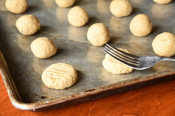 Rolled balls of oatmeal cookie dough on a seasoned cookie sheet  in window light. Fork is flattening them before cooking.