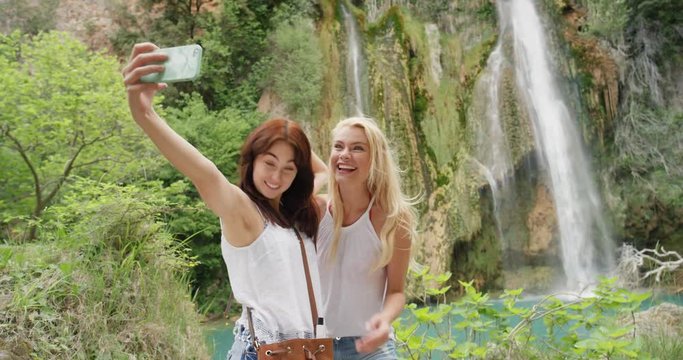 Attractive girl friends taking selfie photograph with smartphone woman enjoying swimming in waterfall nature background view enjoying vacation travel adventure