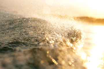 Spray from a breaking wave is illuminated in ethereal, golden light during sunset in this close up image.