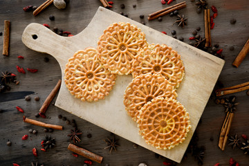 Italian waffle cookies on a textured surface on a cutting board surrounded with spices
