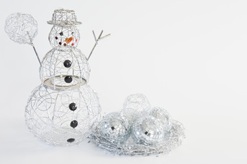 A silver wire snowman with a ball in it's hand and mosaic mirror and wrapped wire balls in a nest made of star garland