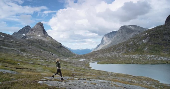 Woman with arms raised on top of mountain looking at view of glacial valley Hiker Girl wearing green down jacket lifting arm up celebrating landscape enjoying vacation travel adventure nature Norway