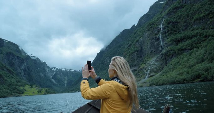 Tourist Woman taking photograph in stormy weather on Fjord Norway with smartphone photographing scenic landscape nature background view enjoying vacation travel adventure