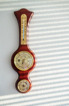 Golden steel red wooden vintage barometer hanging on white wall at home in sunlight. Play of light and shade casted by sun shutters forming parallel lines. Concept background