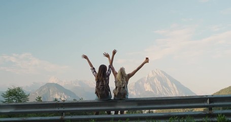 Two young Woman with arms raised on top of mountain looking at view Best friends lifting arm up celebrating scenic landscape  enjoying vacation travel adventure nature Alps Italy