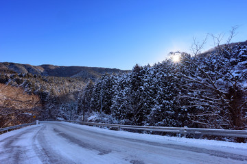 凍結した冬の山の道路を照らす太陽